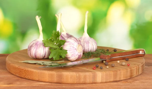Young garlic on cutting board with greenery, pepper and knife on wooden table on green background — Stock Photo, Image