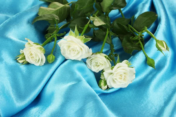 Wunderschöne weiße Rosen auf blauem Satin in Nahaufnahme — Stockfoto