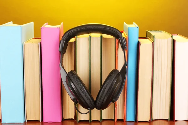 Hörlurar på böcker om träbord på gul bakgrund — Stockfoto