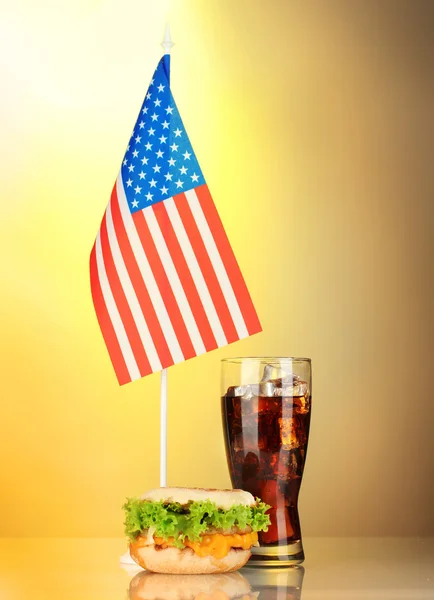 Sanduíche saboroso e cola com bandeira americana, no fundo amarelo — Fotografia de Stock