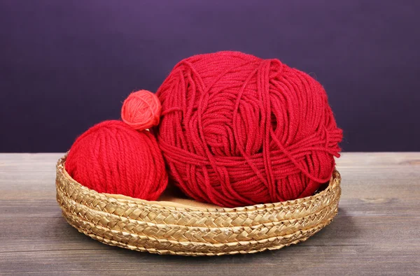 Red knittings yarns in basket on wooden table on purple background — Stock Photo, Image