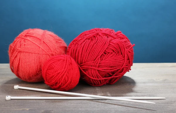 Red knittings yarns on wooden table on blue background — Stock Photo, Image