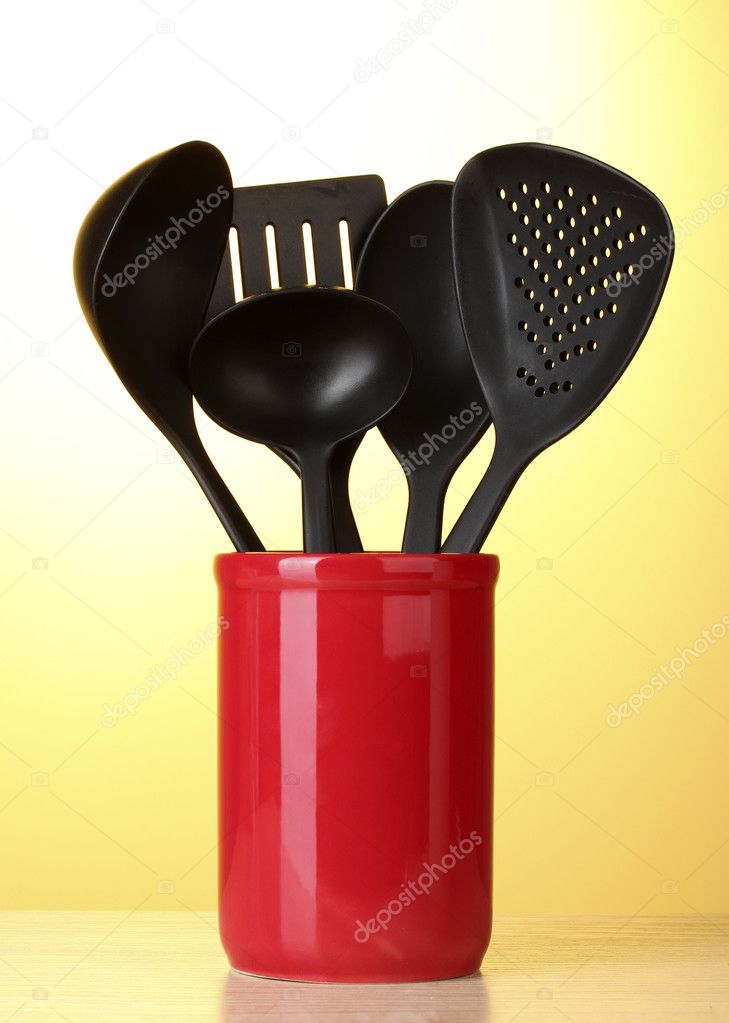 Black kitchen utensils in red cup on yellow background