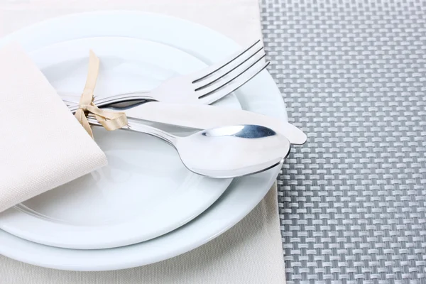 Weiße leere Teller mit Gabel, Löffel und Messer, die mit einer Schleife auf einer grauen Tischdecke gebunden sind — Stockfoto