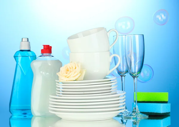 Prázdné čisté talíře, sklenice a kelímky s saponátů a houby na modrém pozadí — Stock fotografie