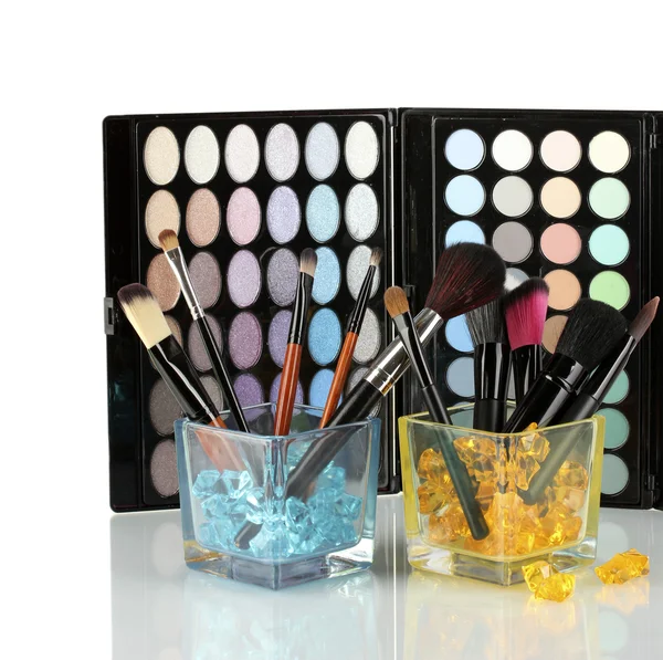 Pincéis de maquiagem em dois copos de vidro com pedras na paleta de sombras de fundo — Fotografia de Stock