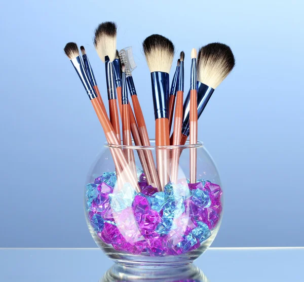 Cepillos de maquillaje en un tazón con piedras sobre fondo azul — Foto de Stock