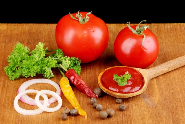 Ketchup and ripe tomatoes on wooden table on black background — Stock Photo, Image