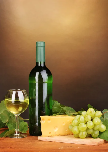 Flasche großer Wein mit Glas und Käse auf Holztisch auf braunem Hintergrund — Stockfoto