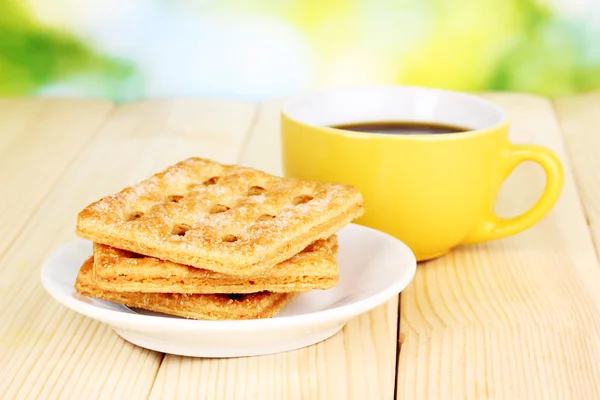 Tasse Kaffee und Kekse auf Holztisch vor hellem Hintergrund — Stockfoto