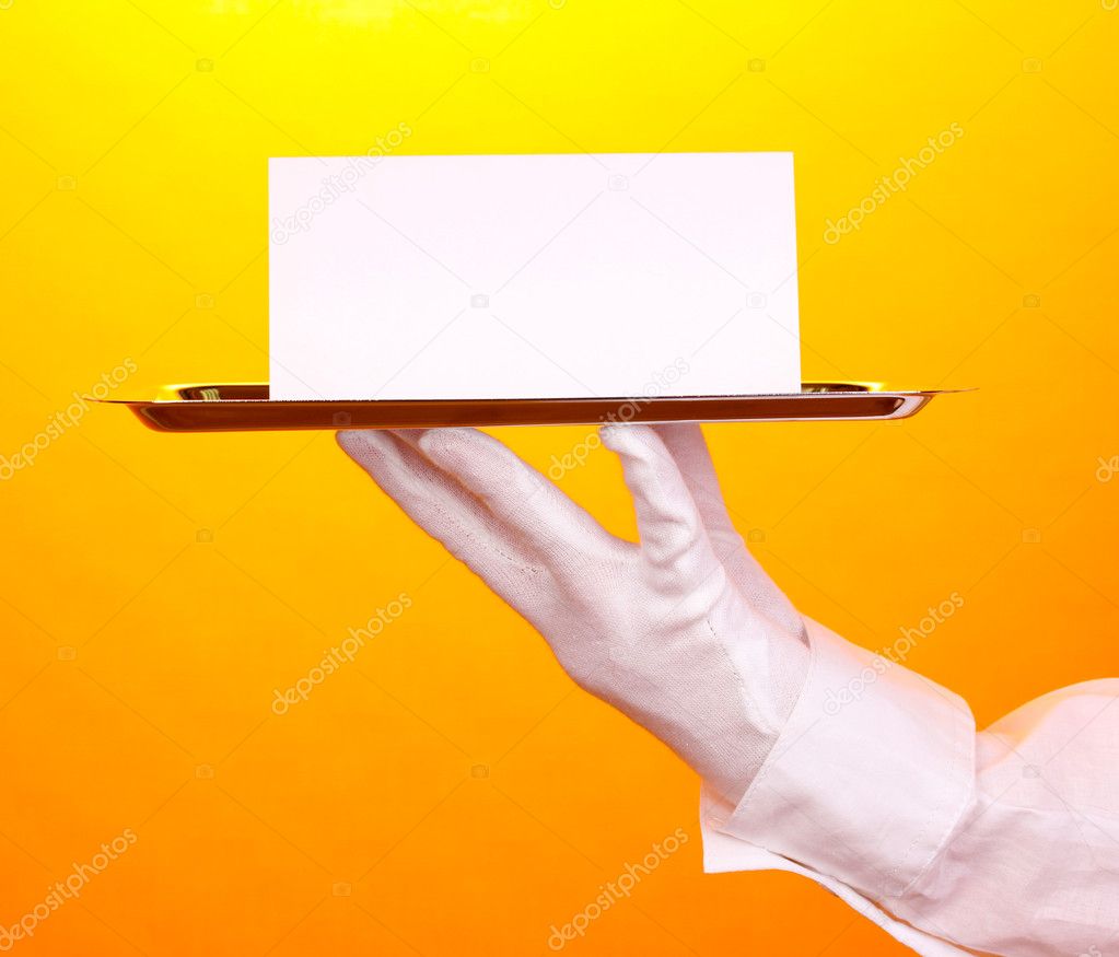 Hand in glove holding silver tray with blank card on yellow background
