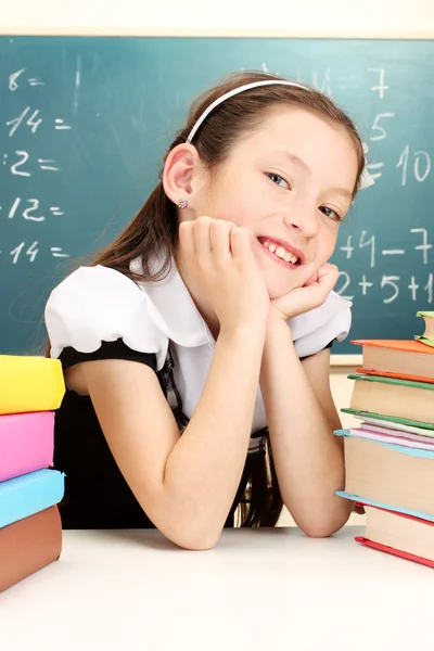 Little schoolgirl and books in classroom near blackboard — Stock Photo, Image