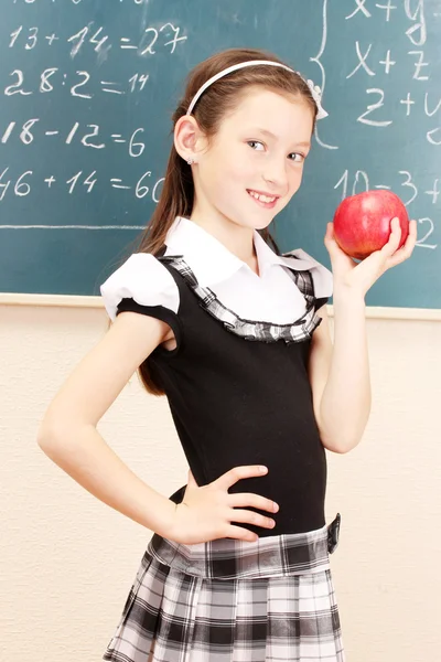 Vacker liten flicka i skoluniform med apple i klassrummet — Stockfoto