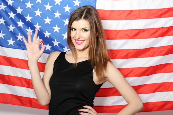 Schöne junge Frau mit der amerikanischen Flagge auf dem Hintergrund Stockbild