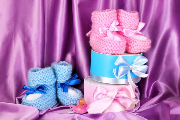 Buty dla dzieci różowy i niebieski, smoczek i prezenty na tle jedwab — Zdjęcie stockowe