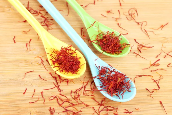 Stigmas of saffron in colorful spoons on wooden background close-up — Stock Photo, Image