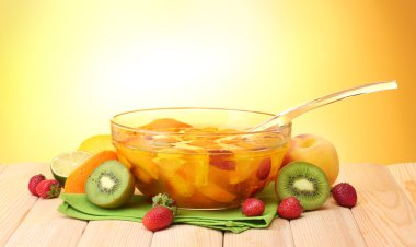 Punch in glass bowl with fruits, on wooden table, on yellow background clipart