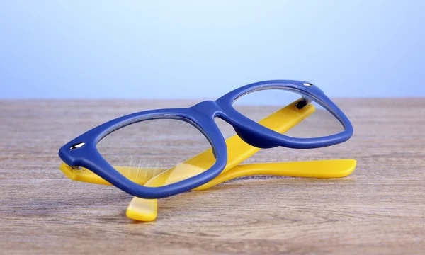 Okulary piękny kolor na drewnianym stole na niebieskim tle — Zdjęcie stockowe