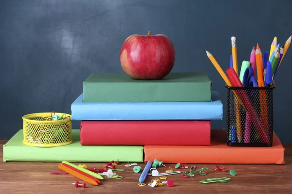 Sammansättningen av böcker, pappersvaror och ett äpple på lärarens skrivbord i bakgrunden i tavlan — Stockfoto