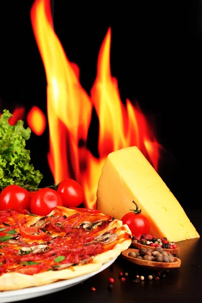 Délicieuse pizza, salami, tomates et épices sur table en bois sur fond de flamme — Photo