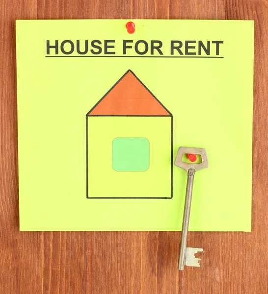 Cartaz sobre alugar a casa com a chave no fundo de madeira — Fotografia de Stock