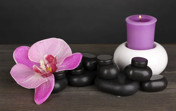 Piedras de spa con flor de orquídea y vela sobre mesa de madera sobre fondo gris —  Fotos de Stock