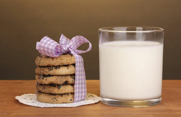 Vaso de leche y galletas sobre mesa de madera sobre fondo marrón —  Fotos de Stock