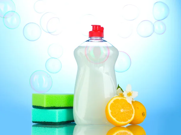 Dishwashing liquid with sponges and lemon with flowers on blue background — Stock Photo, Image