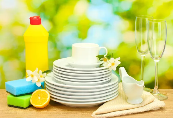 Pratos limpos vazios, copos e copos com líquido de lavar louça, esponjas e limão na mesa de madeira em fundo verde — Fotografia de Stock