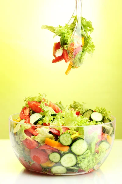 Fresh vegetable salad in transparent bowl with spoon and fork on green background — Stock Photo, Image
