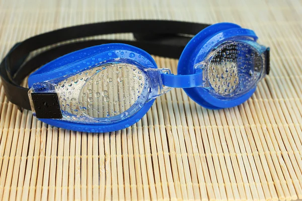Blue swim goggles with drops on a bamboo pad — Stock Photo, Image