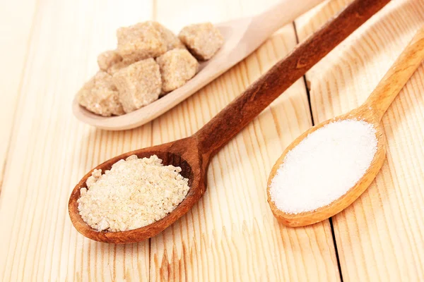 Zucchero bianco e marrone in cucchiai su fondo di legno — Foto Stock