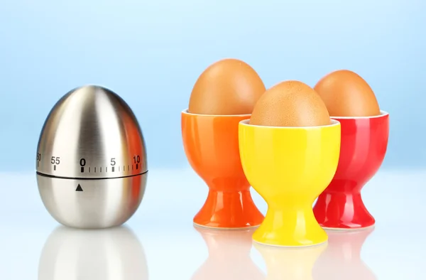 Timer uovo e uovo in stand colore su sfondo blu — Foto Stock