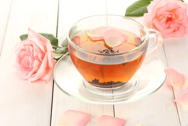 सफेद लकड़ी की मेज पर गुलाब के साथ चाय का कप — स्टॉक फ़ोटो, इमेज