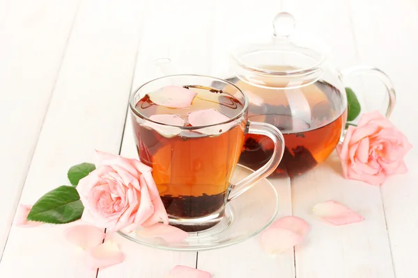 Tetera y taza de té con rosas sobre mesa de madera blanca —  Fotos de Stock