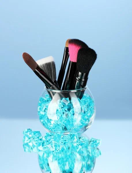 Кисти для макияжа в миске с камнями на синем фоне — стоковое фото