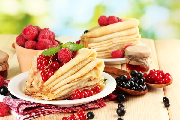 Pancakes with berries, jam and honey on wooden table on green background — Stock Photo, Image