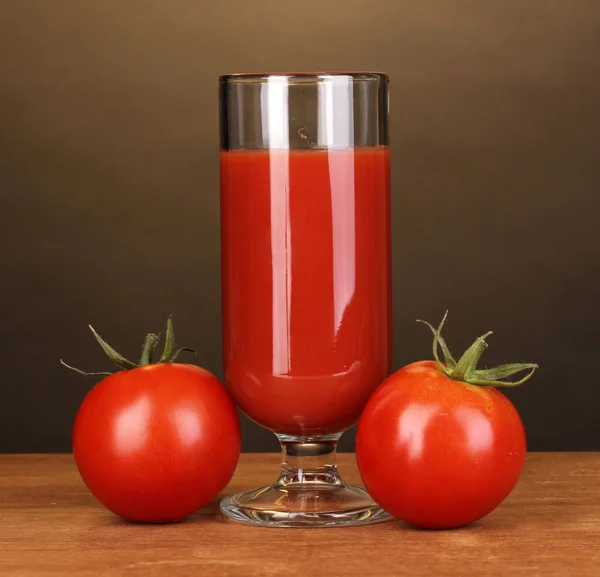 Tomato juice in glass on wooden table on brown background — Stock Photo, Image