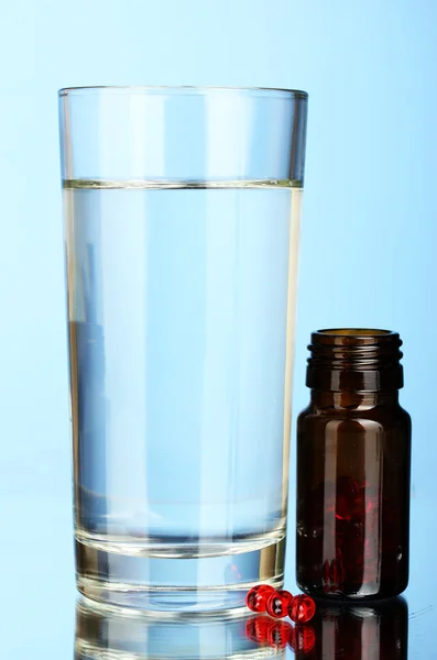 Un vaso de agua y pastillas sobre fondo azul — Foto de Stock
