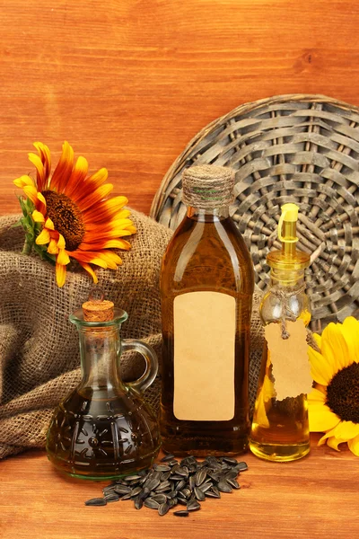 Масло в бутылках, подсолнухах и семенах, на деревянном фоне — стоковое фото