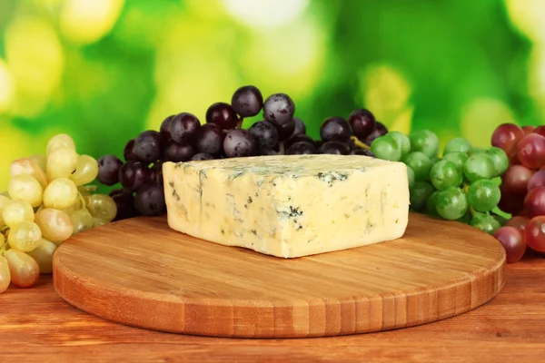 チーズ、まな板の上の明るい緑色の背景でブドウを持つ型 — ストック写真
