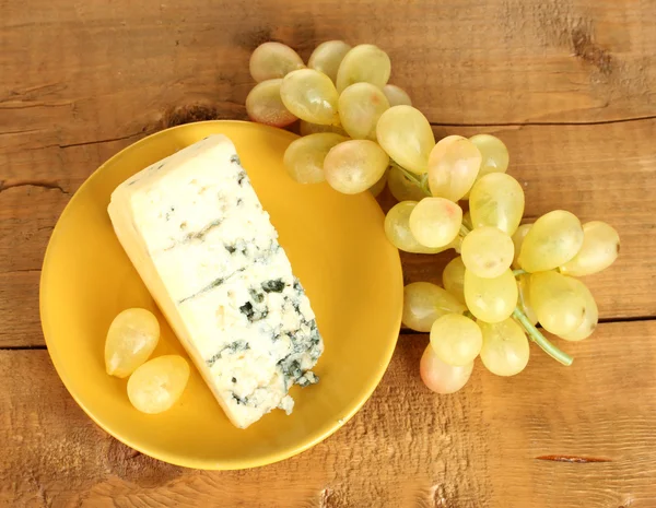 Cheese with mold and grapes on the plate on wooden background close-up — Stock Photo, Image