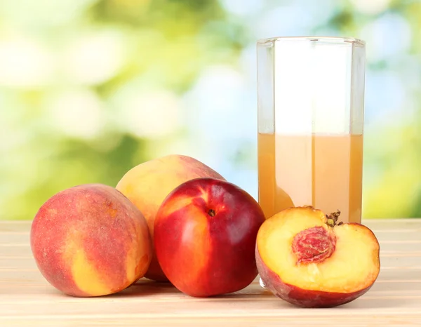 Ripe peaches and juice on wooden table on natural background — Stock Photo, Image