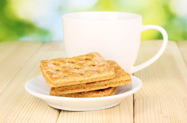 Tasse Tee und Kekse auf Holztisch vor hellem Hintergrund — Stockfoto