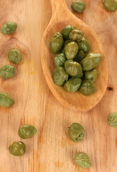 Green capers in wooden spoon on wooden background close-up — Stock Photo, Image