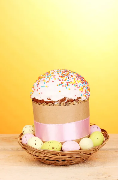 Beautiful Easter cake in basket with eggs on wooden table on yellow background — Stock Photo, Image