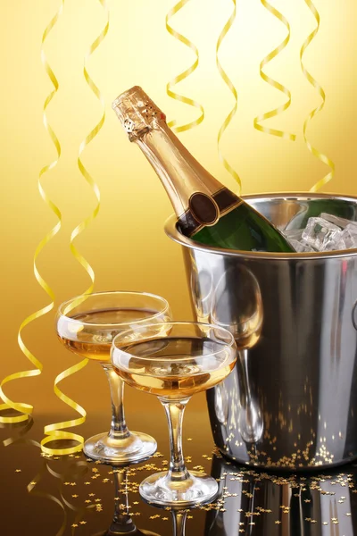 Champagneflaska i hink med is och glas champagne, på gul bakgrund — Stockfoto