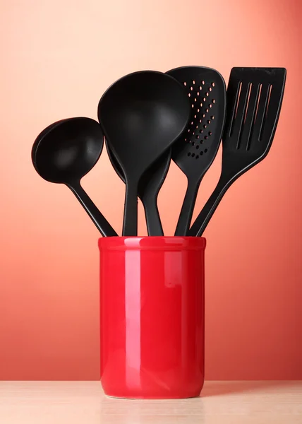 Black kitchen utensils in cup on red bakground — Stock Photo, Image