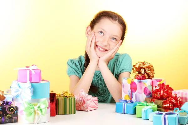 Little girl with gifts on yellow background Stock Photo