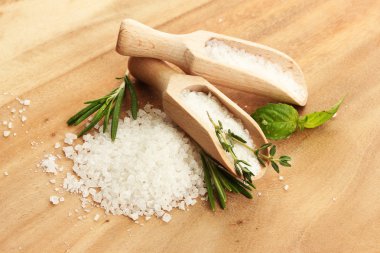 Salt in shovels with fresh basil, rosemary and thyme on wooden background clipart